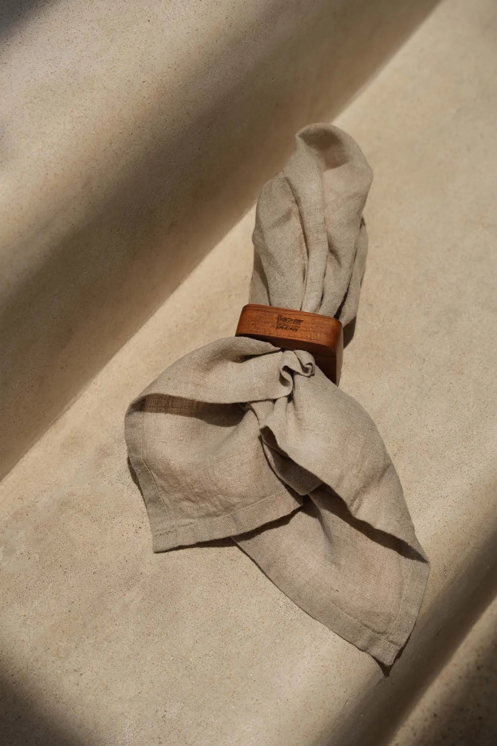 Serviette en lin beige pliée avec anneau en racine de teck naturel