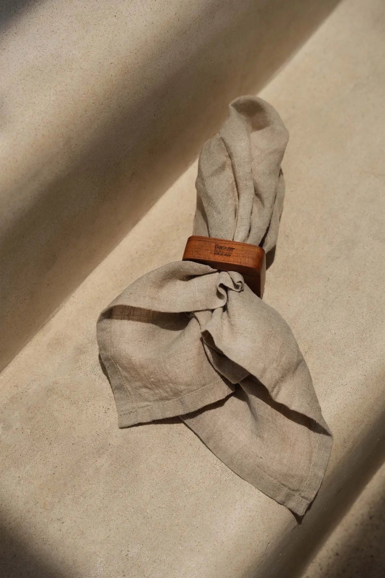 Serviette en lin beige pliée avec anneau en racine de teck naturel