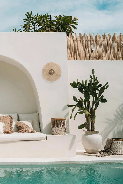 Espace extérieur moderne avec banc, applique murale ronde en rotin et cactus près de la piscine