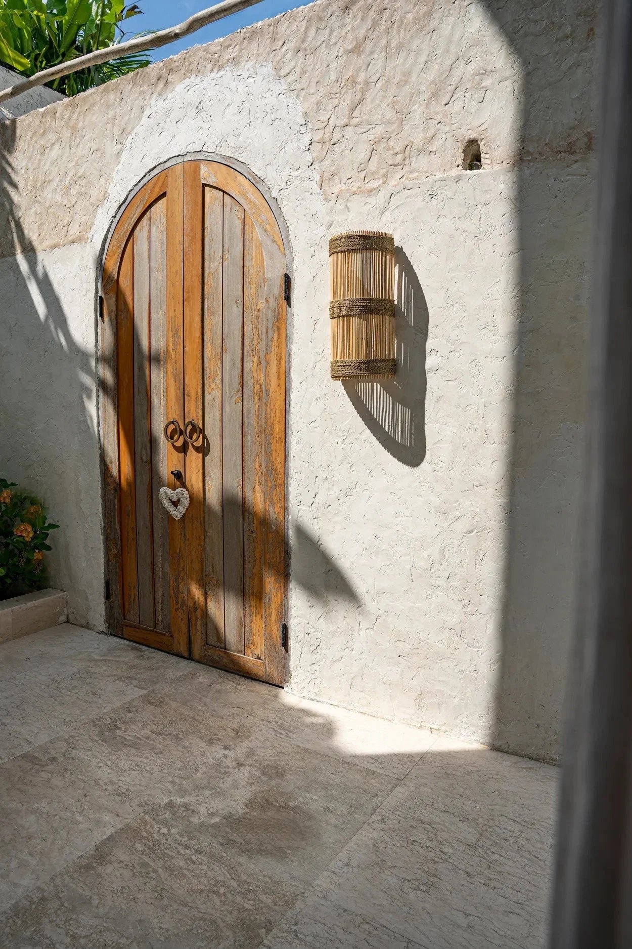 Porte en bois arquée avec poignée en forme de cœur et applique murale en rotin