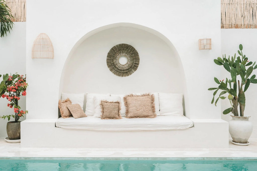 Banc blanc rembourré avec coussins beiges tressés et applique murale rotin conique ajourée H55 cm au-dessus