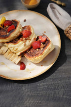Assiette en grès blanc cassé bord doré avec pancakes, fraises, bananes et granola