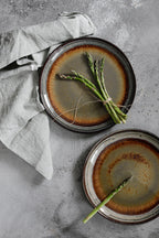 Deux assiettes en grès émaillé brun dégradé, bord texturé, avec asperges fraîches