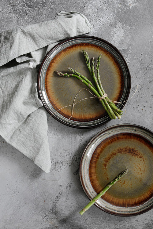 Deux assiettes en grès émaillé brun dégradé, bord texturé, avec asperges fraîches