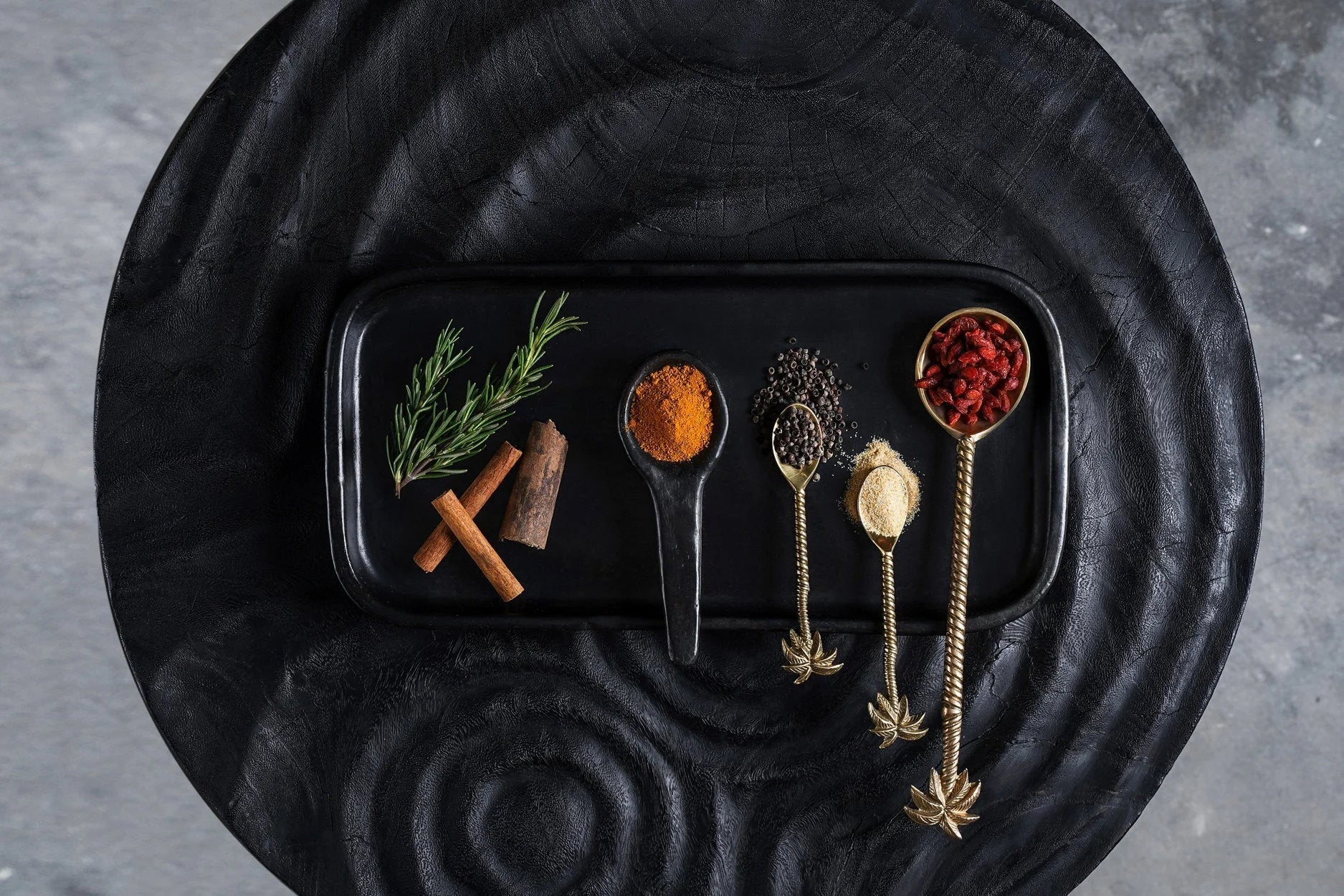 Assiette rectangulaire noire mate avec épices et herbes dans cuillères dorées ornées