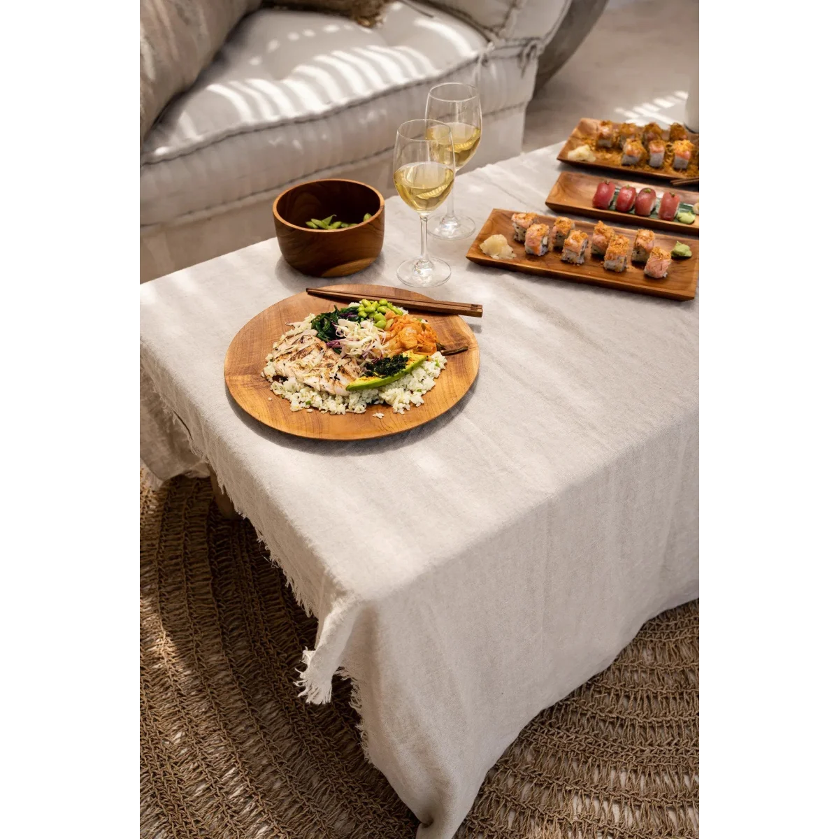 Table en teck massif avec assiette ronde de 30 cm sur nappe en lin blanc à bords effilochés