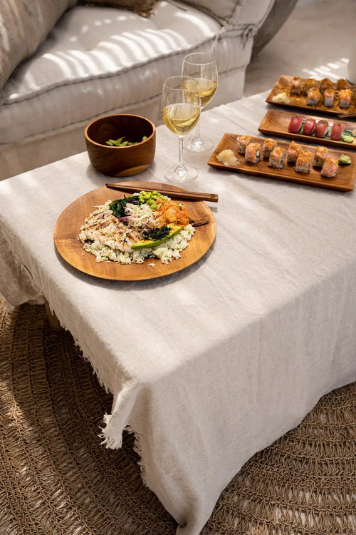 Table en teck massif avec assiette ronde de 30 cm sur nappe en lin blanc à bords effilochés