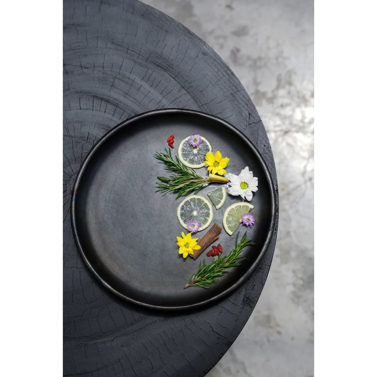 Assiette ronde en terracotta brûlée noir mat Ø30 cm garnie de citron, romarin et fleurs