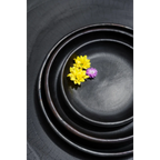 Trois bols en céramique noire avec fleurs jaunes et violettes sur une assiette en terracotta brûlée