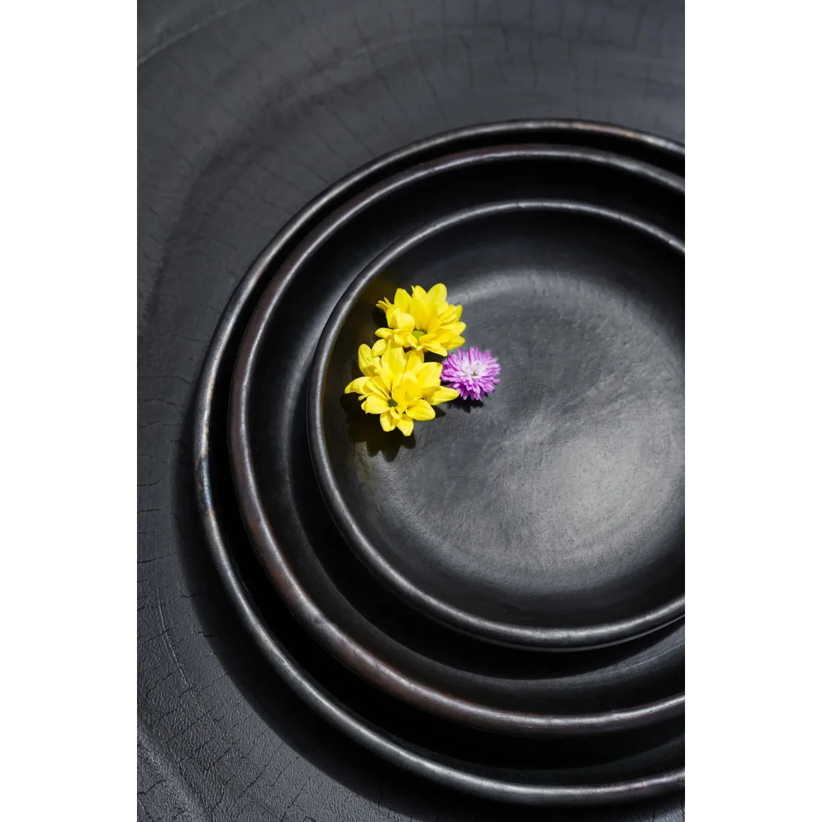 Trois bols en céramique noire avec fleurs jaunes et violettes sur une assiette en terracotta brûlée