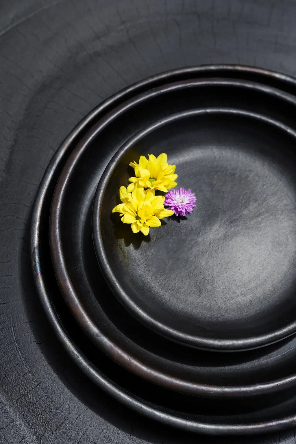 Assiette ronde en terre cuite brûlée noire avec bols en céramique noire et fleurs jaunes et violettes