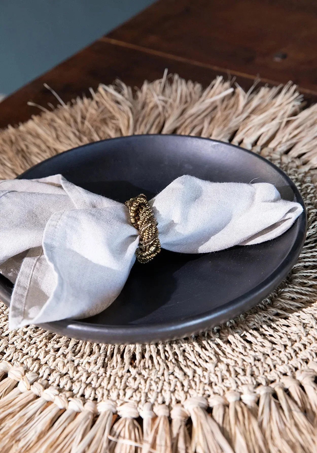Serviette en lin ivoire pliée dans anneau doré sur assiette en terre cuite noire brûlée Ø20 cm