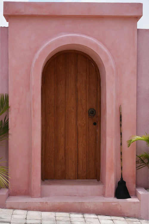 Porte rustique en bois arquée avec poignée en bambou sur mur rose texturé
