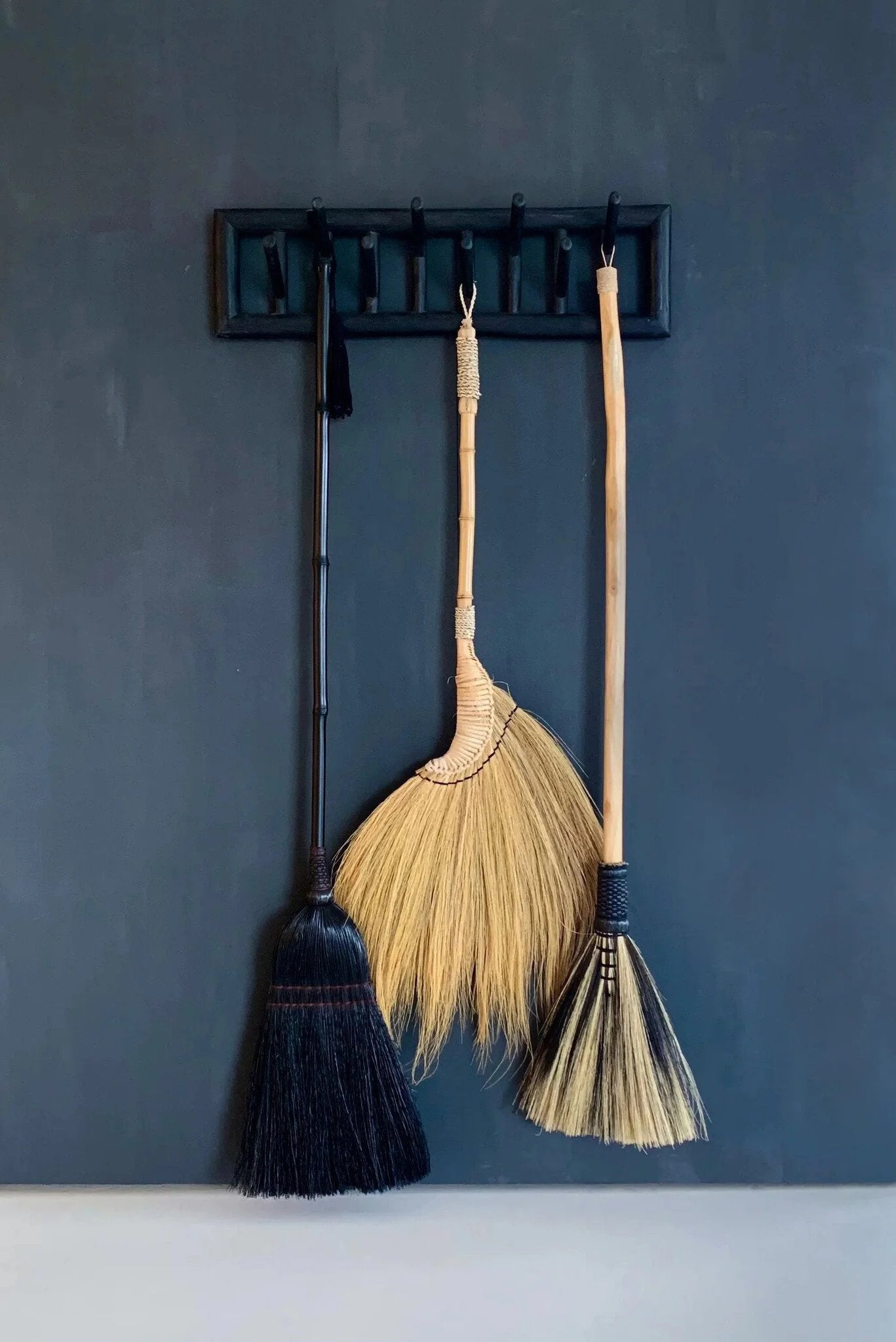 Trois balais décoratifs en fibres noires avec poignée bambou et détails tressés
