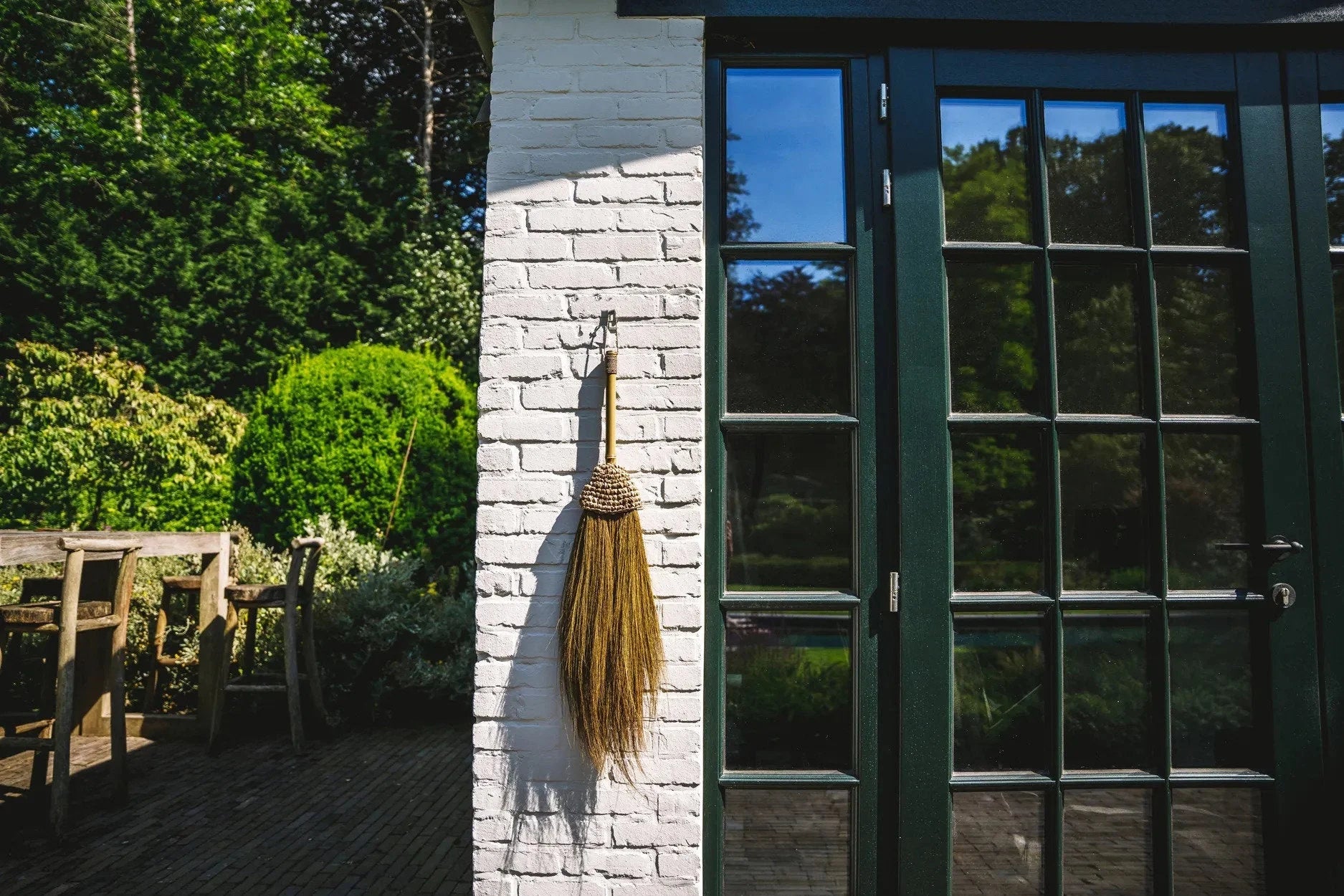 Balai mural décoratif en raphia naturel à franges H75 cm contre mur blanc