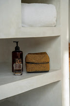 Rangement rectangulaire en perles dorées avec motif géométrique sur étagère de salle de bain