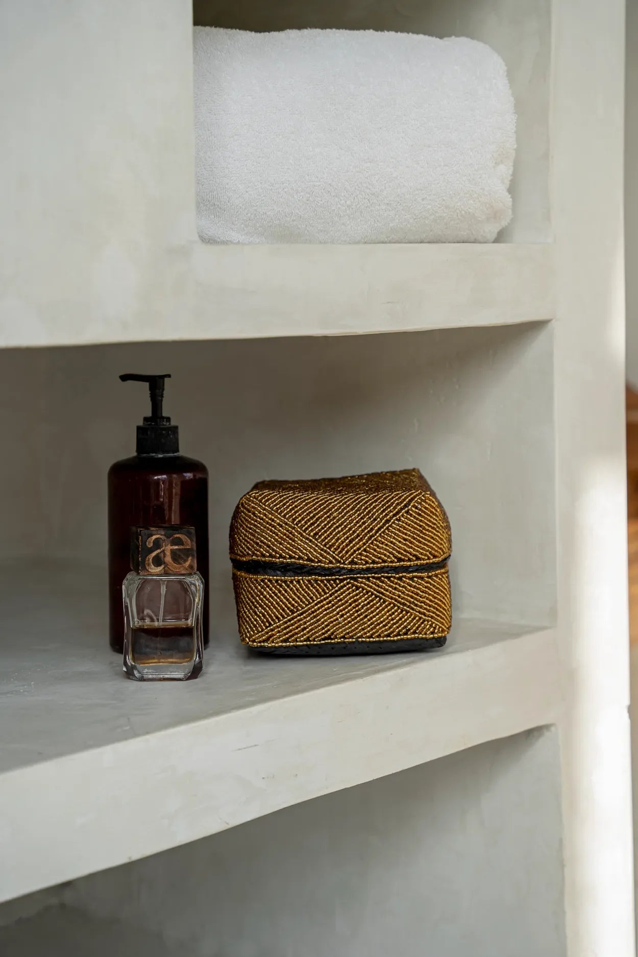 Rangement rectangulaire en perles dorées avec motif géométrique sur étagère de salle de bain