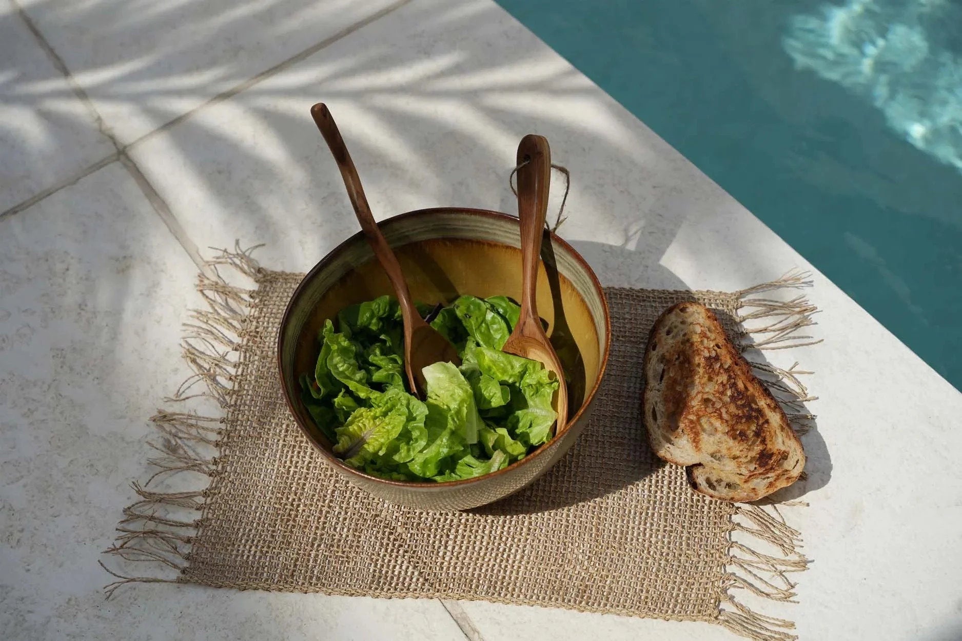 Bol en céramique artisanale blanc cassé et brun avec salade verte et cuillères en bois