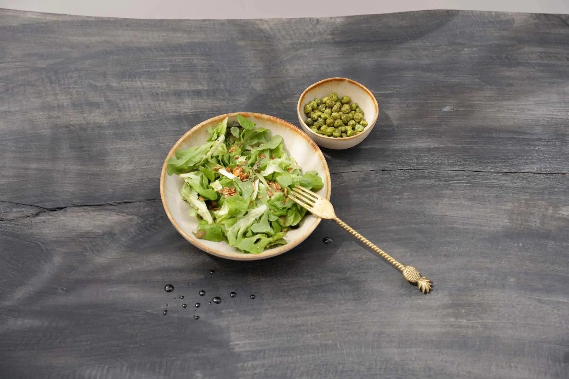 Fourchette à pointe d’ananas doré près d’un bol en céramique crème artisanal de salade et pois verts