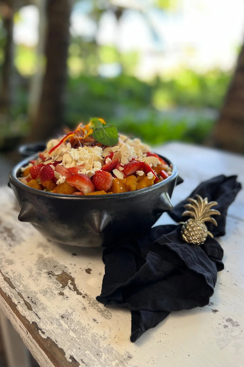 Bol en céramique noire avec reliefs artisanaux, rempli de salade aux fraises, noix et verdure