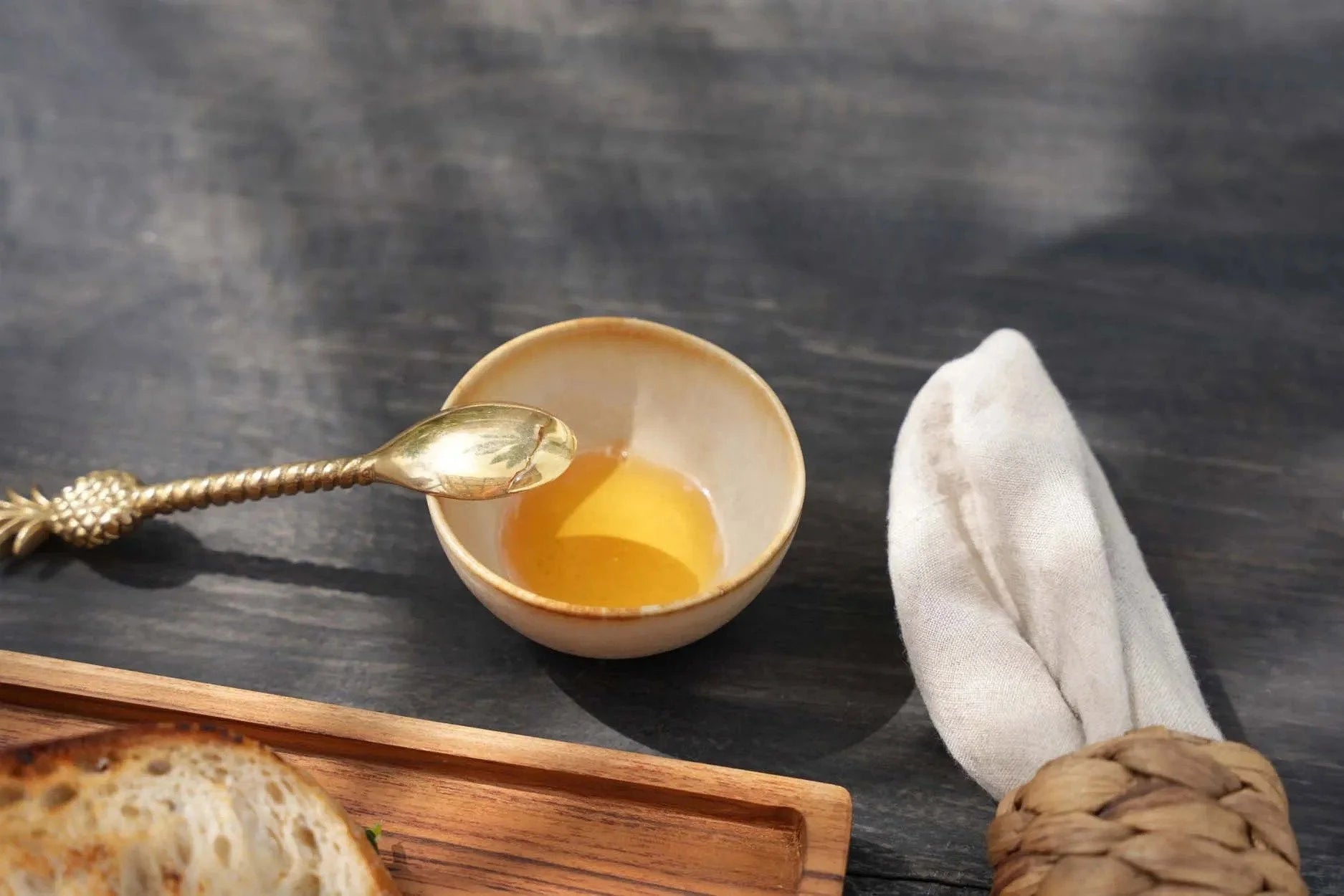 Petit bol en grès beige émaillé bord brun, rempli de miel doré et cuillère à anse ananas dorée