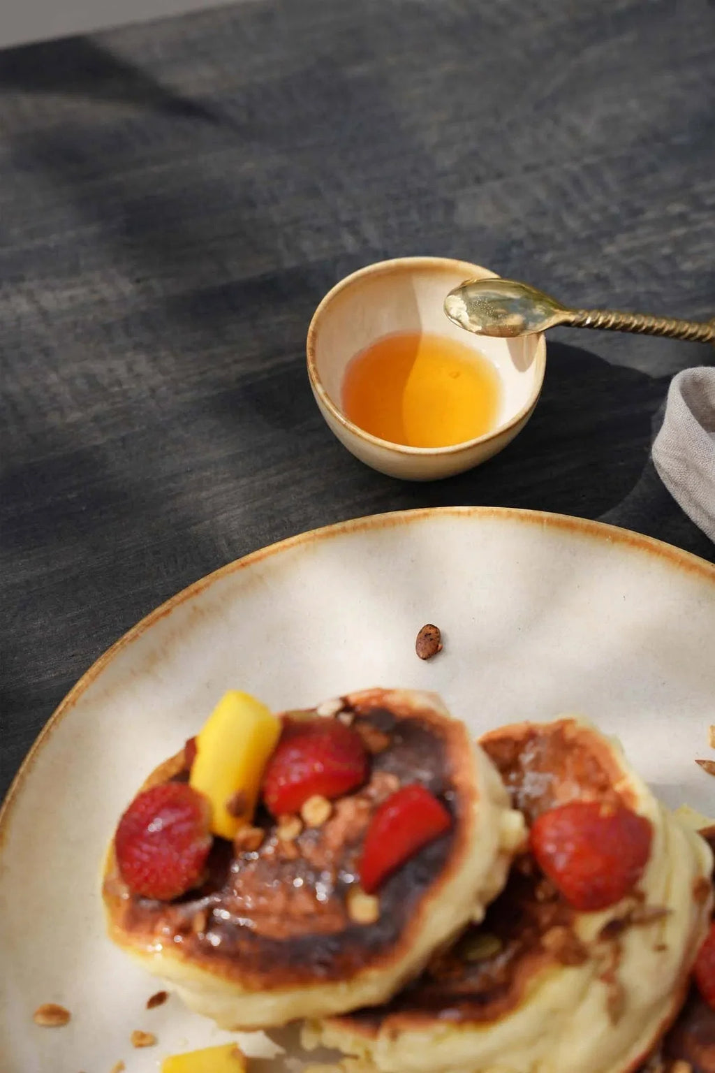 Pile de pancakes dorés aux fraises, mangue et sirop sur bol en grès beige émaillé