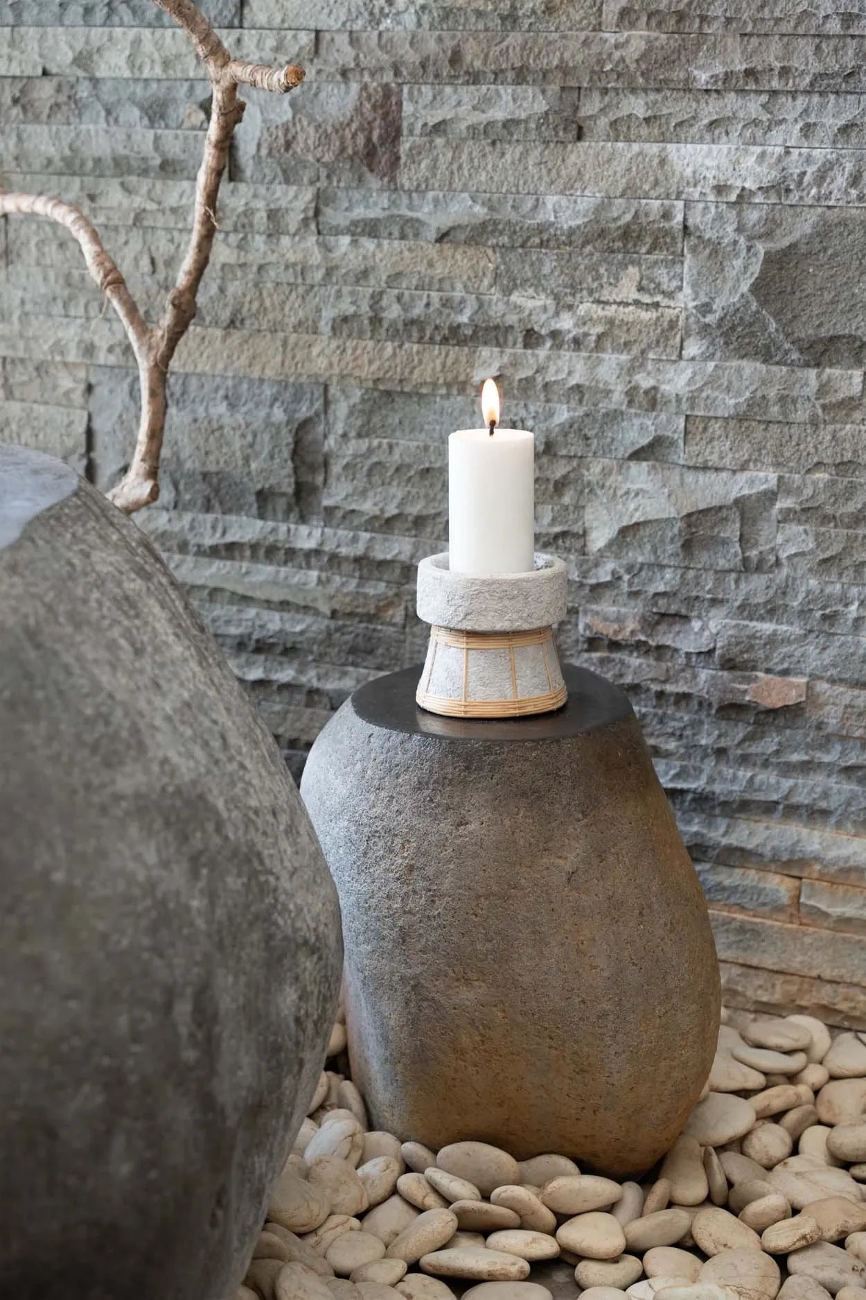 Bougeoir en terre cuite et rotin gris béton avec bougie allumée sur socle en pierre