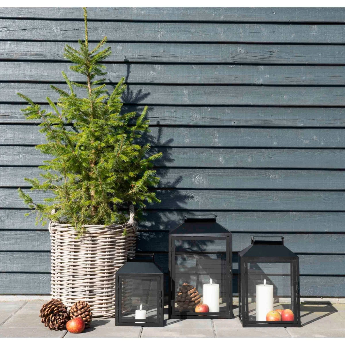 Lanterne en métal noir avec bougies blanches, entourées de pommes et pommes de pin