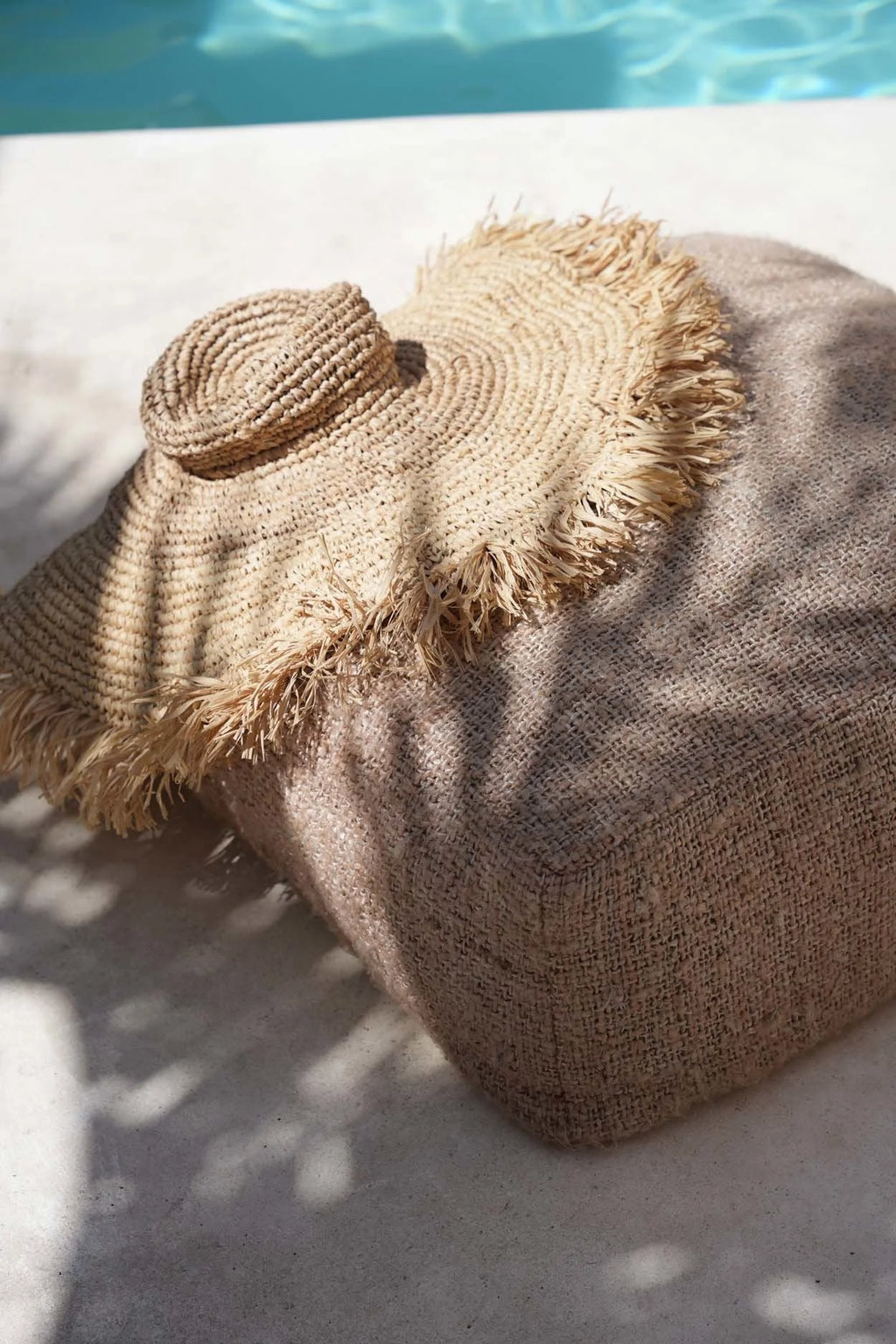 Chapeau en raphia tressé frangé à large bord sur pouf en jute beige