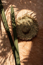 Chapeau en raphia beige frangé, bord large souple contre mur texturé