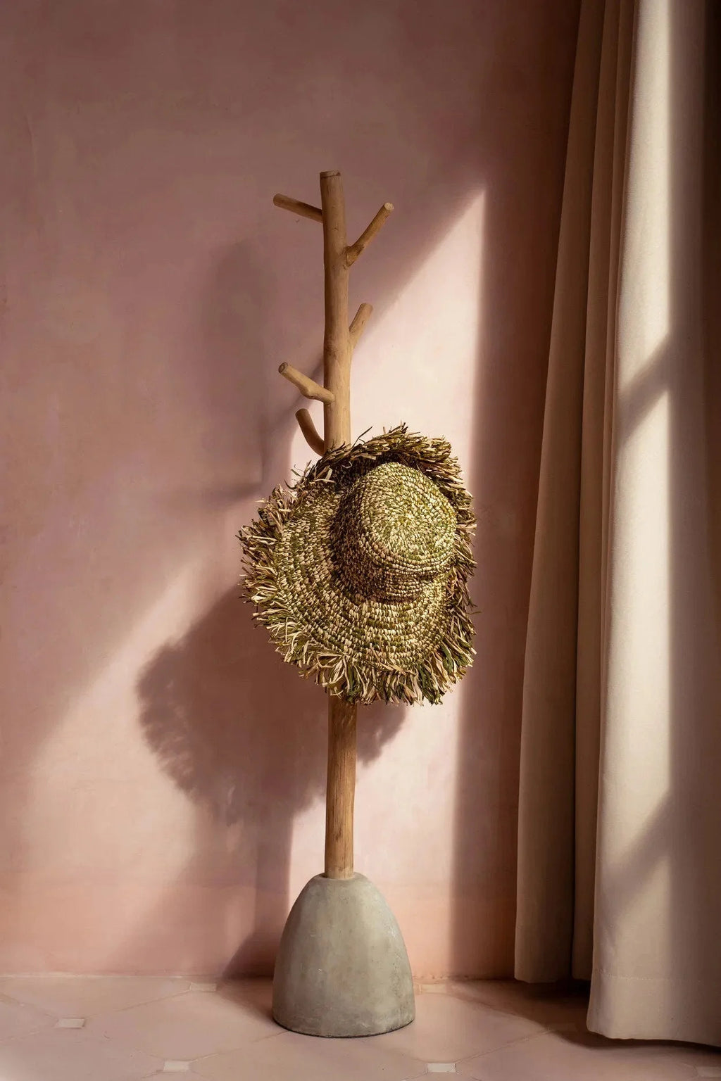 Portemanteau en bois naturel avec base béton tenant chapeau en raphia vert et beige frangé