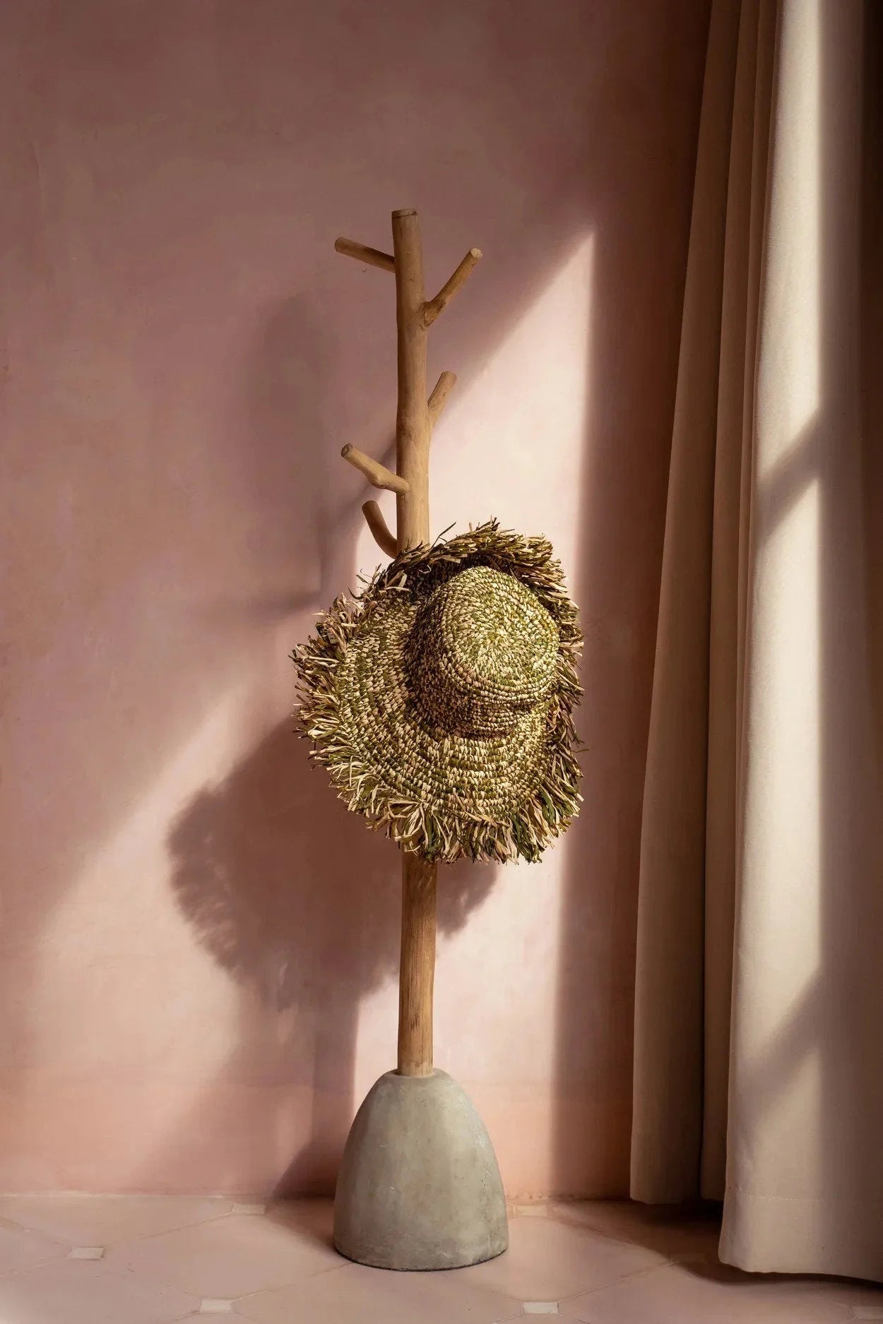 Portemanteau en bois naturel avec base béton tenant chapeau en raphia vert et beige frangé