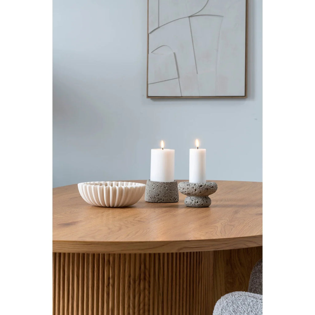 Deux bougies blanches sur piliers dans porte-bougies en pierre grise texturée, table bois