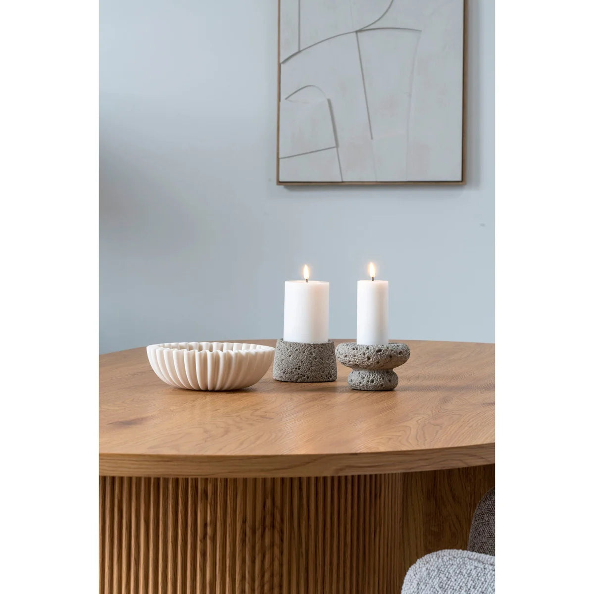 Deux bougies blanches sur piliers dans porte-bougies en pierre grise texturée, table bois