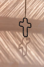 Croix murale décorative en bois noir perlé suspendue à une corde sur mur rose