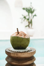 Coconut vert avec paille, prêt à boire, associé à Dessous de plat rond en jonc de mer blanc bordé de coquillages