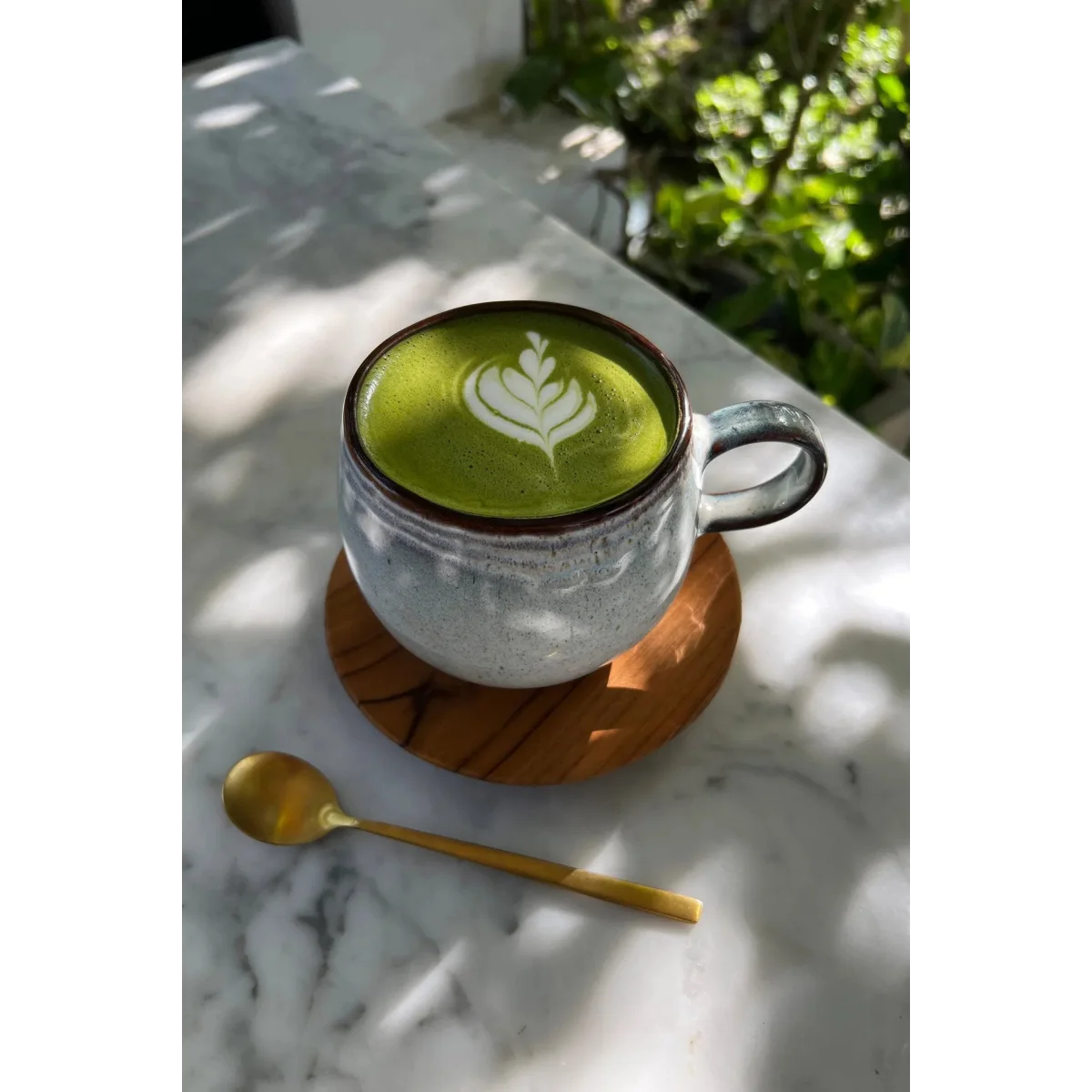 Tasse en céramique vert vif avec latte art blanc et dessous de verre en teck naturel