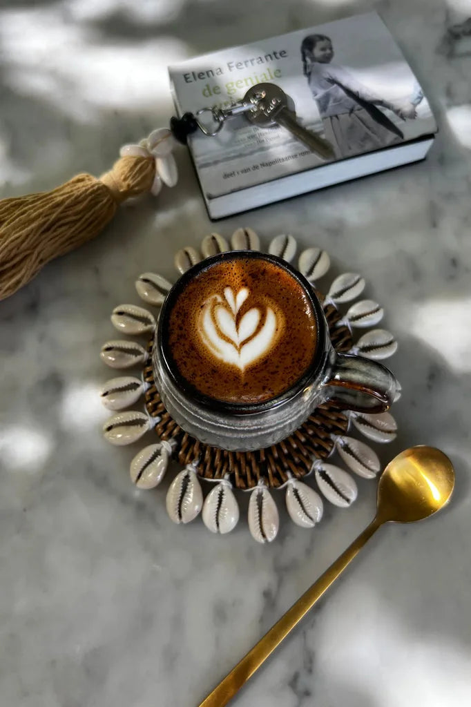 Café latte avec art dans une tasse en verre pour Le dessous de verre colonial en coquillage