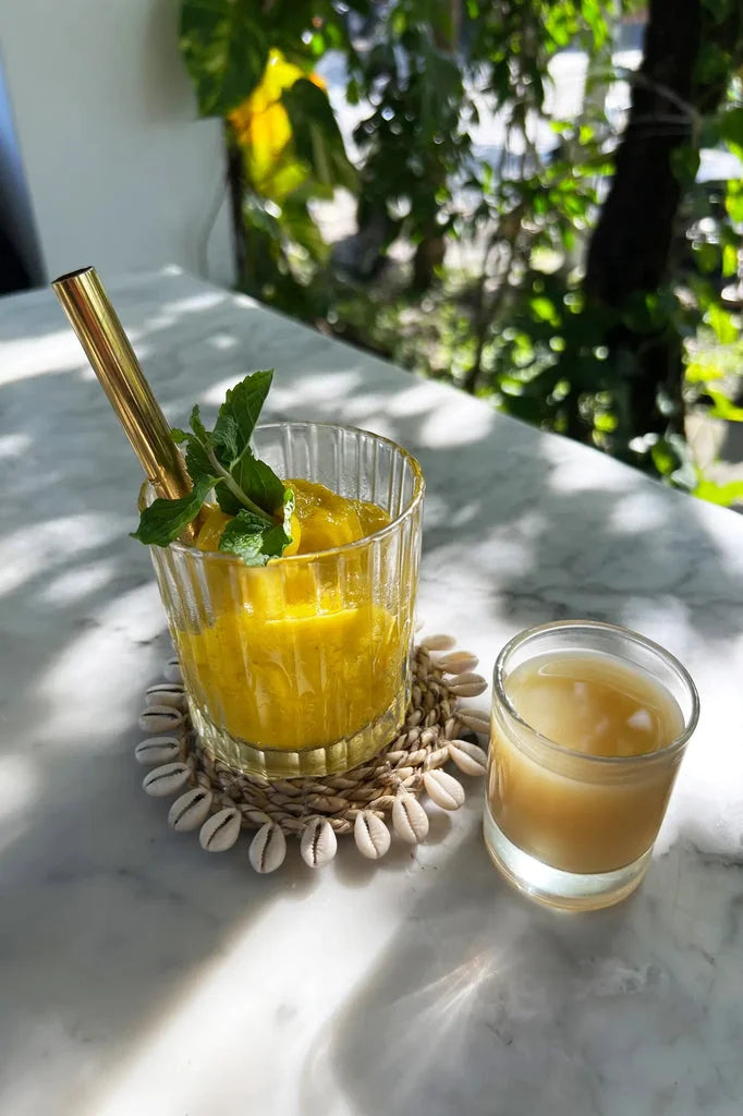 Smoothie jaune rafraîchissant avec paille sur le dessous de verre en coquillage et jonc de mer