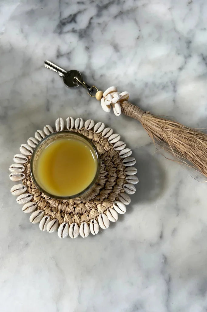 Verre de liquide jaune sur sous-verre en coquillage avec clé et pompon.