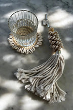 Verre d’eau sur sous-verre en forme de coquillage avec porte-clés en forme de coquillage et de pompon.