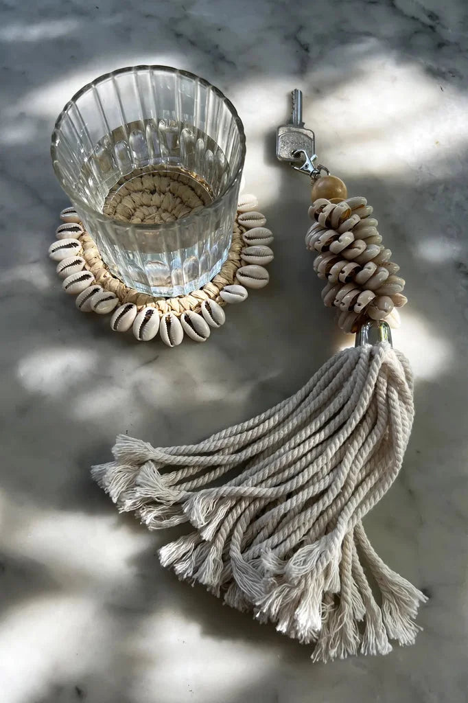 Verre d’eau sur sous-verre en forme de coquillage avec porte-clés en forme de coquillage et de pompon.