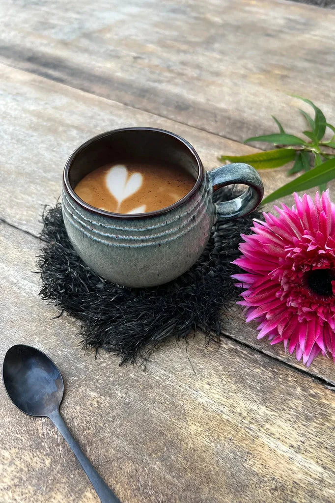 Latte avec motif en cœur dans une mug en céramique, associé à le dessous de verre en raphia noir