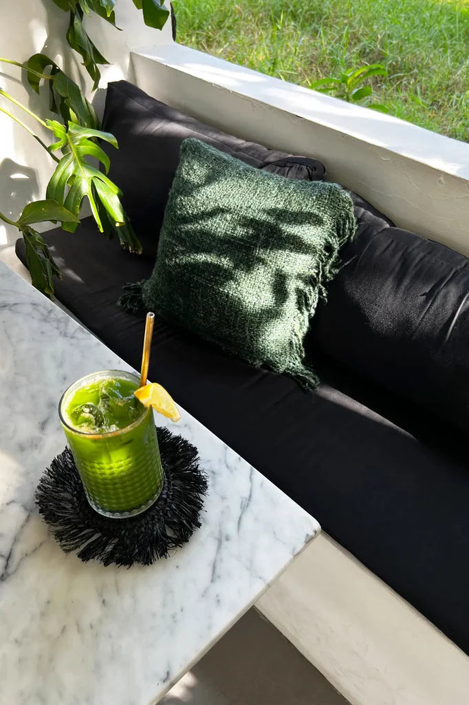 Smoothie vert avec paille et tranche de citron sur le dessous de verre en raphia noir