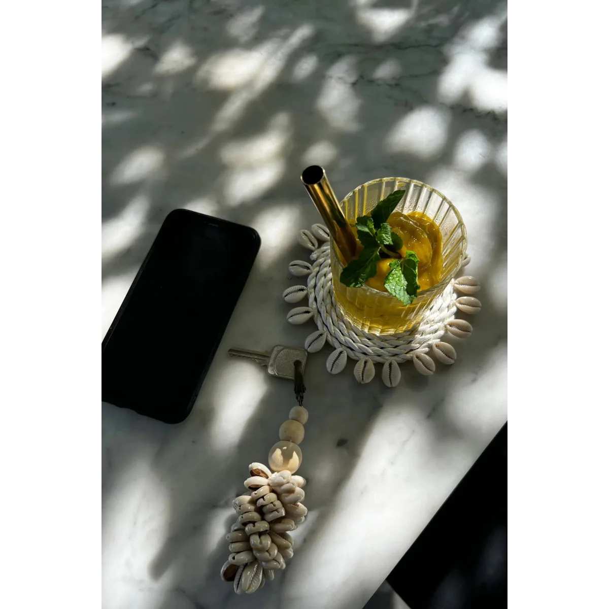 Verre de boisson jaune avec paille en métal et menthe sur un sous-verre en coquillages