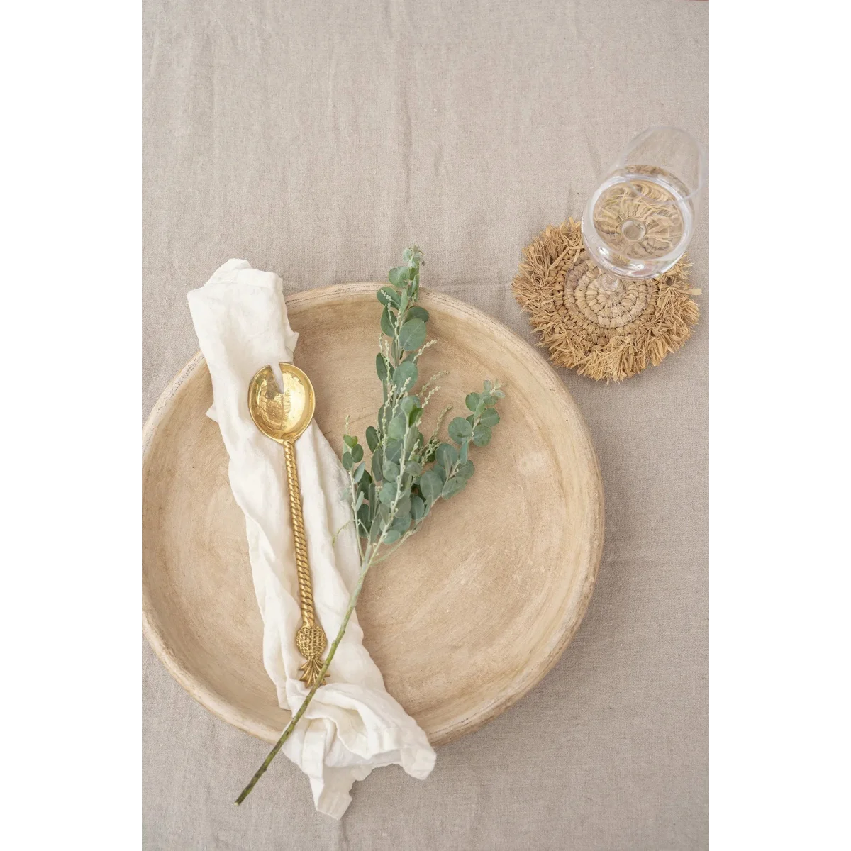 Assiette céramique beige avec cuillère dorée et branche d’eucalyptus verte