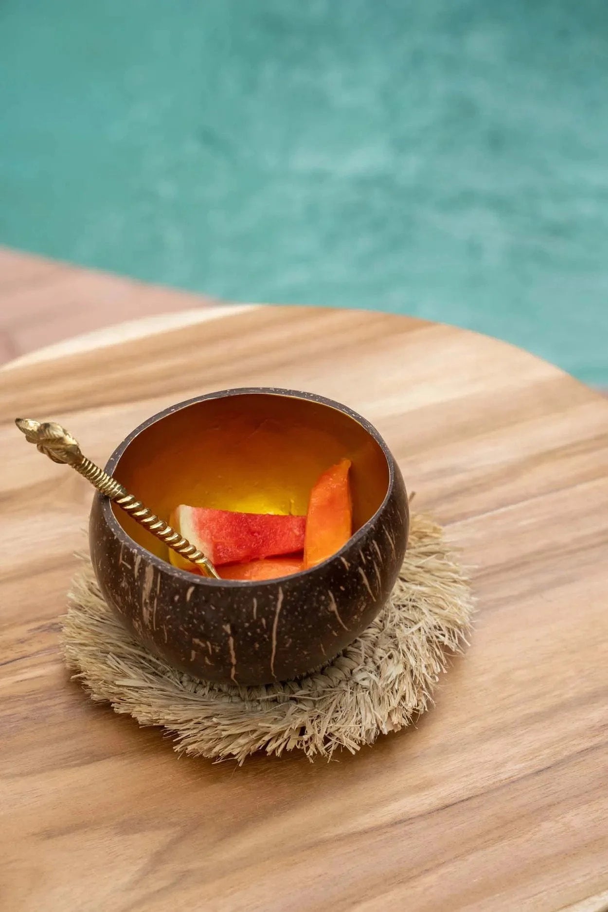 Verre en coque de noix de coco brun avec tranches d’orange et paille sur sous-verre rond en raphia naturel à franges solaires