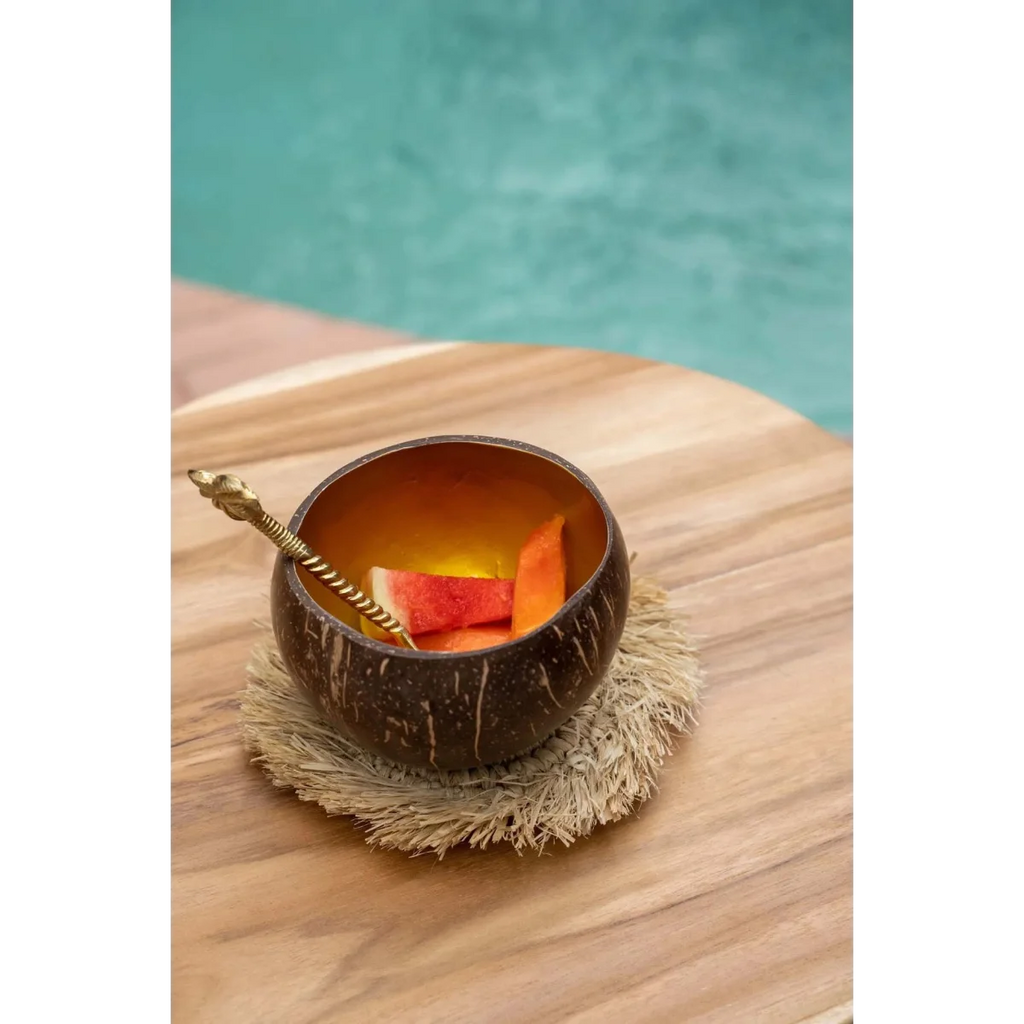 Verre en coque de noix de coco brun avec tranches d’orange et paille sur sous-verre rond en raphia naturel à franges solaires