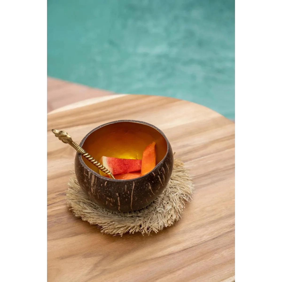 Verre en coque de noix de coco brun avec tranches d’orange et paille sur sous-verre rond en raphia naturel à franges solaires