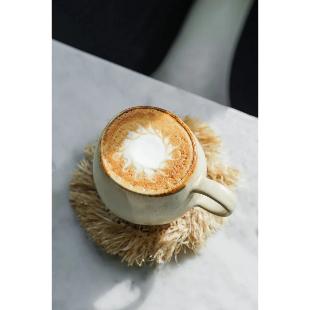 Tasse en céramique crème avec latte art sur sous-verre rond en raphia frangé